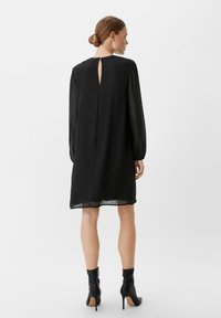 Czarna sukienka z długimi przezroczystymi rękawami, szczegółem w kształcie łezki z tyłu oraz swobodnym krojem. Noszona z dopasowanymi czarnymi botkami za kostkę. Gładka faktura materiału.