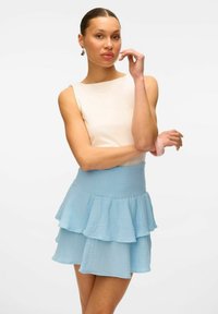 Top bianco senza maniche con una finitura liscia, abbinato a una gonna a strati in tessuto azzurro chiaro con volantin, che mette in risalto una vita aderente.
