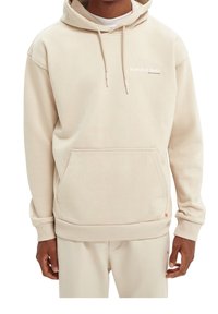 Beige huvtröja med kengurufickor, snörning i huvan, ribbade ärmslut och nederkant. Har en liten vit logga på bröstet och mjuk textur.