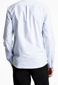 Camicia a maniche lunghe di colore azzurro chiaro con righe bianche verticali, dotata di una piega sul retro e polsini con bottoni, realizzata in un tessuto liscio e intrecciato.