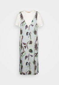 T-shirt blanc à manches courtes superposé sous une robe grise sans manches à col en V avec de grands motifs discrets de tournesols.