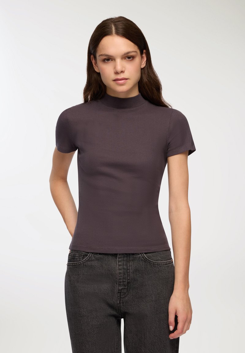 Top a maniche corte, con collo alla coreana, in tessuto a costine grigio scuro, design aderente, abbinato a jeans neri a vita alta, visibili dettagli di texture liscia.