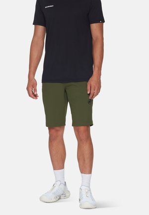 Black short-sleeve shirt with white logo, paired with olive green shorts featuring a round logo patch, and white textured athletic shoes.