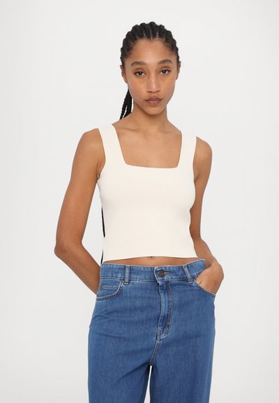 Cream-colored, fitted crop top with a square neckline and thick straps, paired with high-waisted blue denim jeans. Smooth texture.