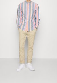 Randig skjorta i flera färger med nyanser av rosa, blått och grått, med en knapp-upplagad krage, som bärs med beige chinos och vita sneakers.