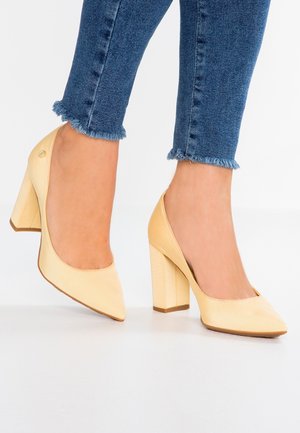 Żółte satynowe szpilki z ostrym noskiem i masywnym obcasem. Buty mają gładką teksturę i minimalistyczny design.