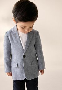 Helles blaues Leinenblazer mit Reverskragen, Ein-Knopf-Verschluss und zwei vorderen Taschen, getragen über einem weißen Hemd und dunklen Hosen.