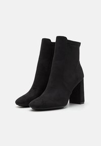 Stivali alla caviglia in finta suede nera con una texture liscia, punta a mandorla e tacco chunky. Design elegante con dettagli di cucitura minima.