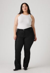 Black denim flared jeans with front pockets, a button closure, and contrasting stitching, paired with a white ribbed tank top.
