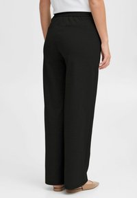 Black wide-leg pants with an elastic waistband, soft texture, and side pockets. The back features a single pocket detail.