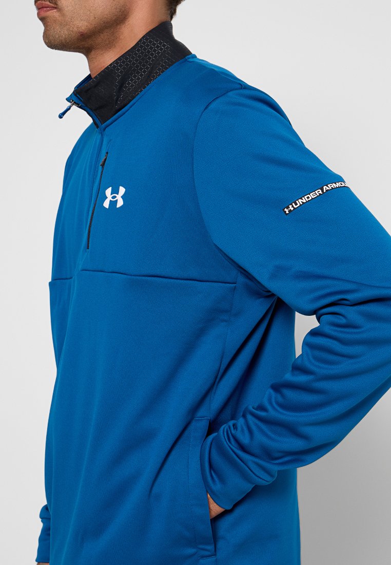 Pull-over de sport bleu à demi-zip avec un col noir, arborant un logo blanc sur la poitrine et la manche, fabriqué en tissu léger et texturé.