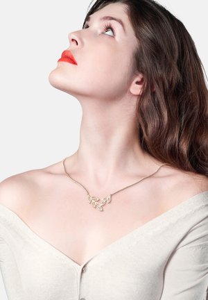 Goldblatt-Pendel-Halskette an einer zarten Kette, mit einem symmetrischen Design und sanft zugespitzten Blattformen. Modell trägt einen leichten Pullover.