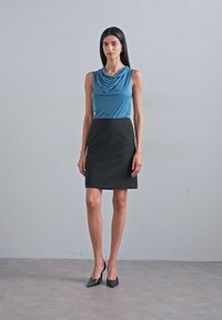 Blå draperad topp i kombination med en figursydd svart kjol och svarta högklackade skor; slät tygtextur, rena linjer och modern silhuett.