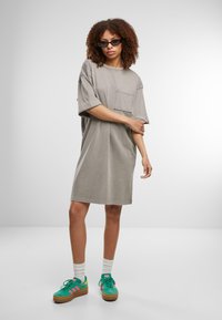 Siva oversized T-shirt haljina s džepom na prsima, ležeran dizajn. Nosena uz zelene tenisice i bijele čarape za opušten izgled.