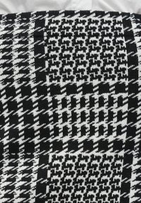 Strickstoff mit einem schwarz-weißen geometrischen Muster, das abwechselnd Karos und Hahnentritt-Designs aufweist, samtige Textur.