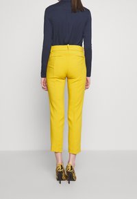 Gele getailleerde broek met een slim fit en achterzakken, gecombineerd met een marineblauwe top met lange mouwen en gemusterde hoge hakken.