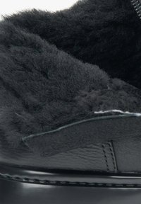 Zwarte leren schoen met een fuzzy zwarte voering en een gladde textuur, met een subtiele steekdetail langs de rand.