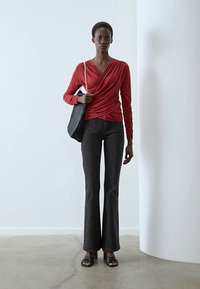 Red long-sleeve top with a draped design, paired with black flared jeans and black heeled sandals. Black shoulder bag with chain strap.