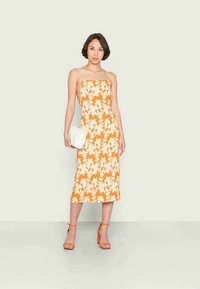 Vestido midi com padrão floral laranja e alças spaghetti, combinado com uma bolsa branca e sandálias de salto laranjas. Tecido suave e design ajustado.