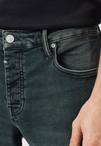 Tmavě zelené džíny z denimu s hladkou texturou, designem s pěti kapsami a stříbrným kováním na pase a kapsách.