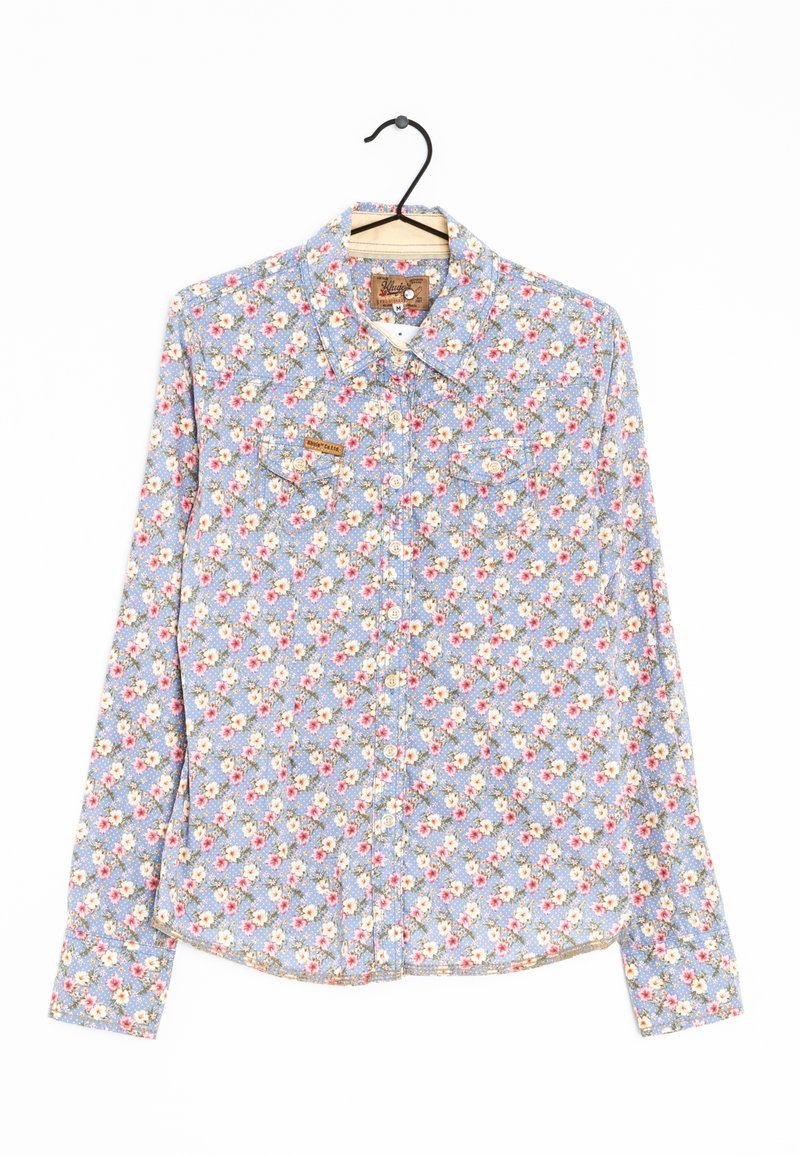 Camicia blu a maniche lunghe con motivo floreale, con chiusura a bottoni e due tasche sul petto. Il tessuto appare texturizzato con piccoli fiori colorati.