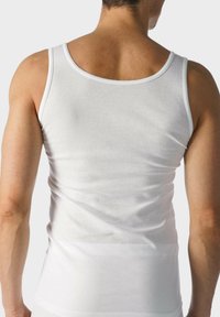 Biały bawełniany top na ramiączkach o klasycznym kroju, gładkiej teksturze i dopasowanym fasonie. Ramiączka są szerokie, a dekolt okrągły.