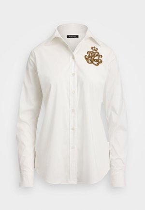 Biela košeľa na gombíky so štruktúrovaným golierom a dlhými rukávmi. Obsahuje zlatú vyšívanú monogramovú ozdobu na ľavej hrudi.