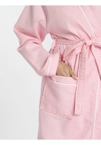 Peignoir de bain rose en texture gaufrée, avec une taille ceinturée, présentant des bordures blanches et une poche avant. Axé sur le confort et la fonctionnalité.