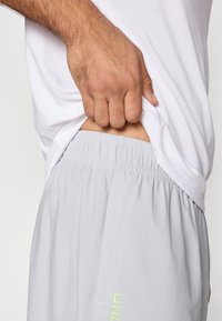 Light gray athletic shorts with an elastic waistband and side pockets, featuring a subtle logo detail in neon yellow.