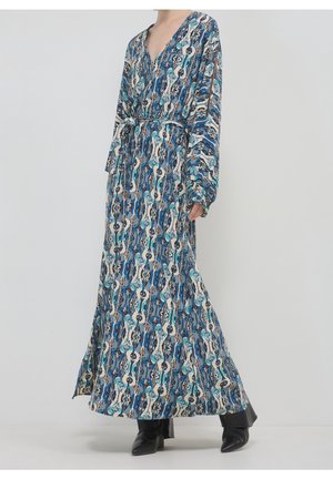 Langes blau-weiß gemustertes Kleid mit langen Ärmeln und gebundener Taille, getragen mit schwarzen spitzen Stiefeln.