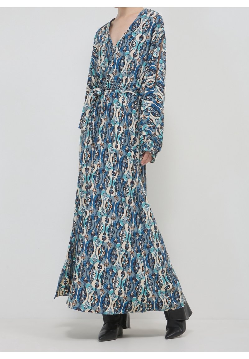 Robe longue bleue et blanche à motifs, manches longues et taille nouée, portée avec des bottes noires pointues.