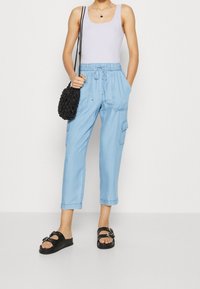 Light blue, cotton blend cargo pants with elastic waistband and drawstring, featuring side pockets. Paired with black sandals and a small bag.