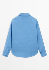 Lyseblå skjorte med lange ærmer set bagfra med spids krave og manchetter med knapper på hvid baggrund.