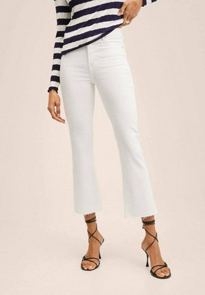 Vrouw draagt witte high-waisted flare jeans met rafelige zomen, zwarte sandalen met hoge hakken en bandjes, en een marineblauw-wit gestreept shirt met lange mouwen.