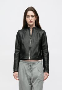 Jaqueta bomber preta de couro com gola alta e fecho de correr frontal. Apresenta linhas elegantes e um design cropped. Combina com calças cinza claro.