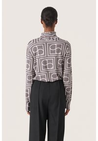Langärmliges Hemd in Grau mit einem geometrischen weißen Muster, ausgestattet mit einem hohen Kragen und weichem Material; kombiniert mit lockeren schwarzen Hosen.