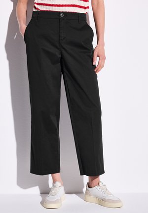 Black cropped pants in cotton twill with side pockets, a button closure, and a relaxed fit, paired with light-colored sneakers.