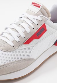 Tenisky Puma s horní částí z lehké šedé a bílé síťoviny, červenými akcenty a béžovou semišovou špičkou. Bílé tkaničky a hnědá pryžová podrážka.