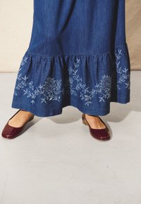 Denim maxi krilo z nabranim robom, okrašeno z modrim cvetličnim vezenjem. V kombinaciji z burgundskimi balerinkami.