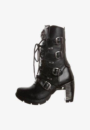 Botte en cuir noir montant jusqu'au genou avec lacets, cinq boucles ajustables, talon texturé et accent strié. Présente des détails en métal poli.