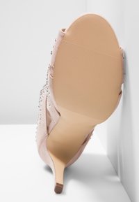 Stiletto de ante beige con un tacón alto y una suela texturizada en marrón claro. Presenta brillantes coloridos a lo largo del lado y un diseño de parte trasera abierta.