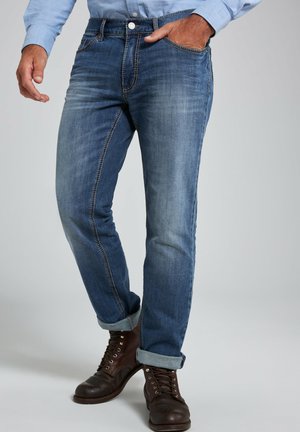 Blue denim jeans with light and dark wash effects, five-pocket design, tapered fit, and turned-up cuffs. Brown lace-up boots complement the look.