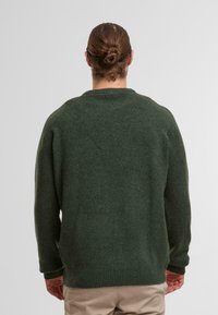 Donkergroen sweater gemaakt van zacht breiwerk, met een ronde hals, lange mouwen en geribbelde manchetten en zoom. Comfortabele, relaxte pasvorm.