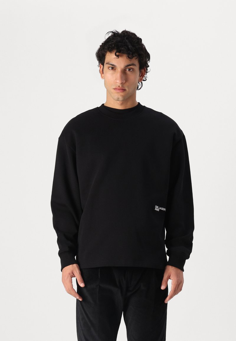 Sweatshirt negru cu guler rotund și mâneci lungi, având un detaliu cu logo în partea stângă jos. Fabricat dintr-un material moale și texturat.