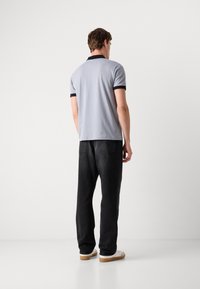 Lys grå polo med svart krage og ermeikoner, sammen med mørke svarte jeans og hvite sneakers. Enkelt design, avslappet passform.