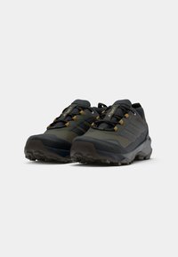Scarpe da trail running con una parte superiore grigia e verde oliva, tessuto testurizzato, design con lacci e una suola nera robusta per una migliore trazione.