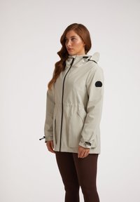 Lichtgrijze waterdichte jas met een capuchon, ritssluiting, verstelbare manchetten, elastische taille en een zwart logo op de mouw.