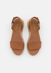 Sandali di pelle marrone con due larghe cinghie, suola in sughero a zeppa e rifinitura intrecciata. Fibbia regolabile alla caviglia per una vestibilità sicura.