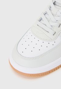 Hvit lær sneakers med perforert tåboks, flate grå snøringer og gummigummi såle. Har et lite sølvfarget logoakzent.