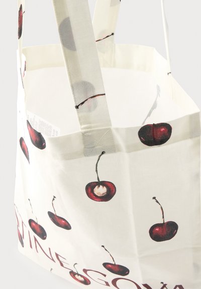 Sac fourre-tout en tissu blanc avec des illustrations de cerises rouges et des anses larges, montrant une partie du texte imprimé près du bord inférieur.